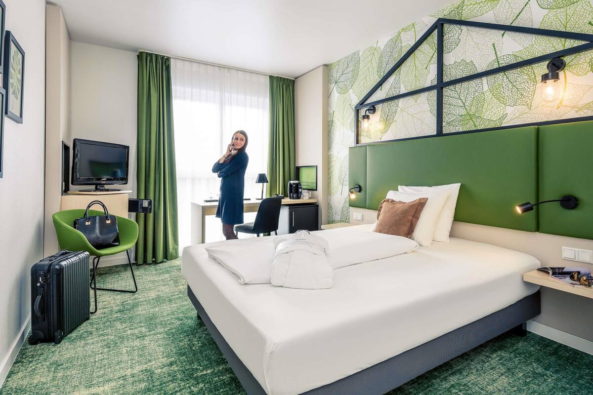 Una habitación de hotel con una cama grande, un escritorio con una silla, un televisor y una silla verde.
