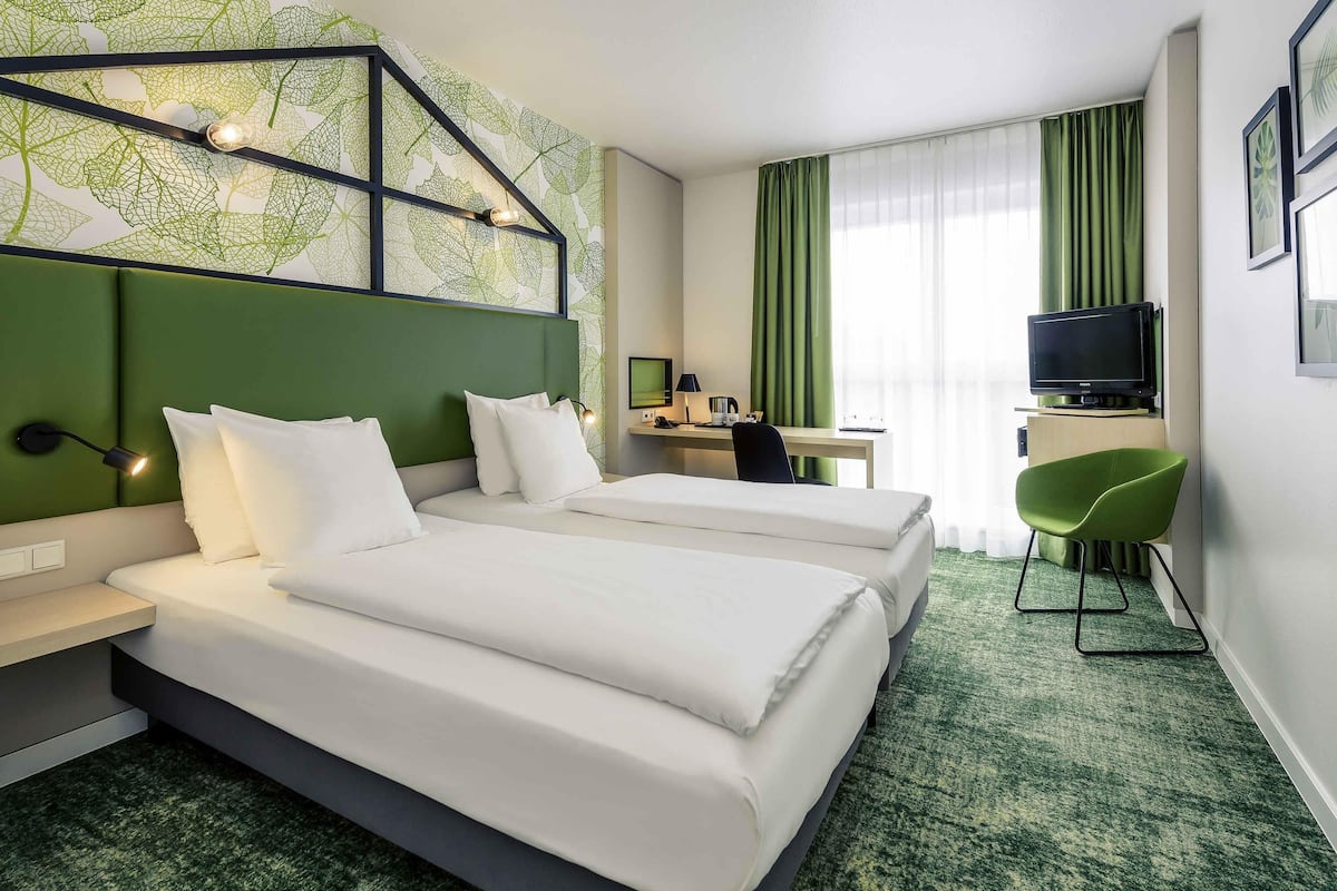 Habitación de hotel con dos camas, un escritorio, una silla, un televisor y una alfombra verde.