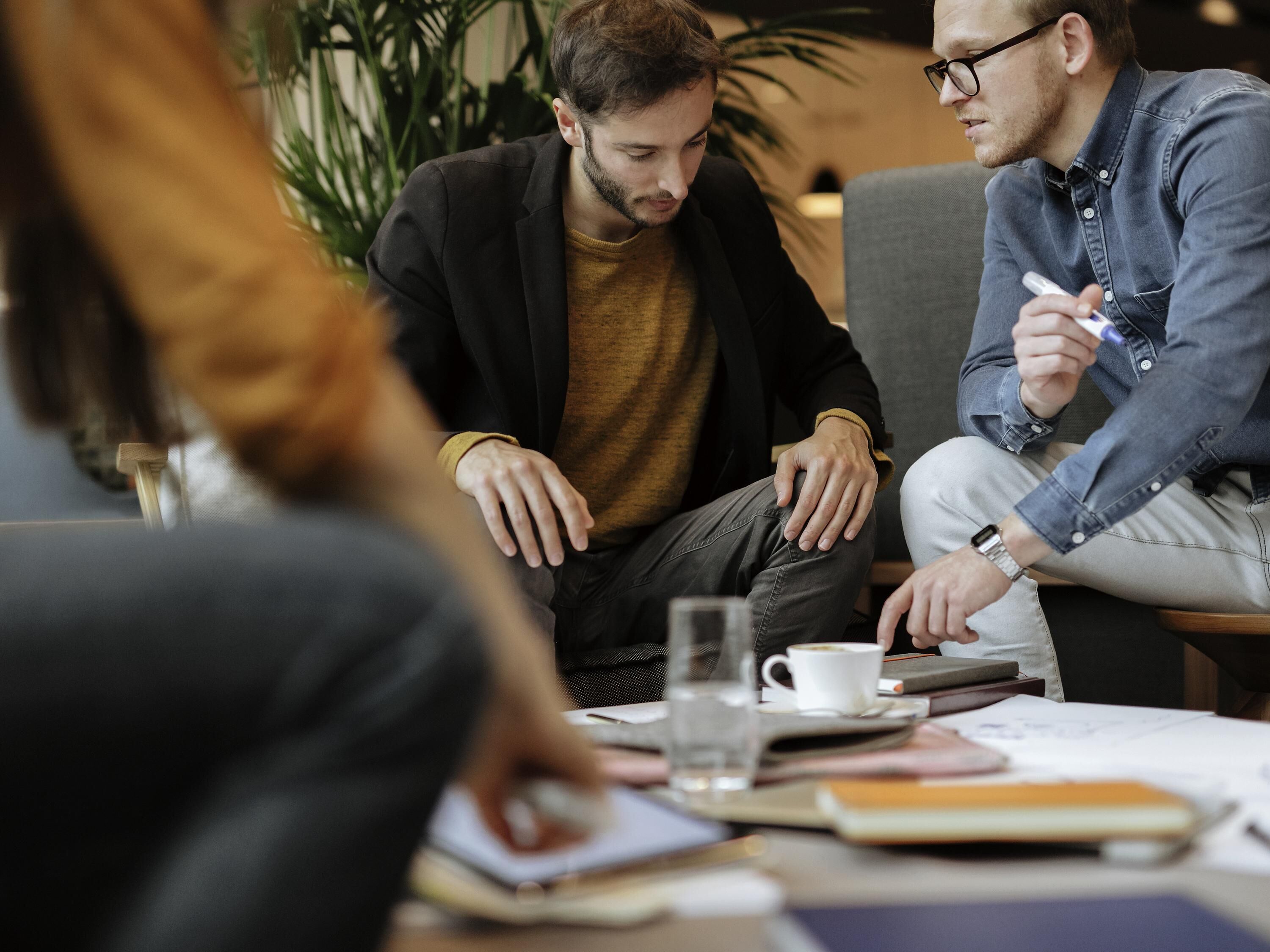 A group of people in a meeting room with a table, notebooks, and a cup.