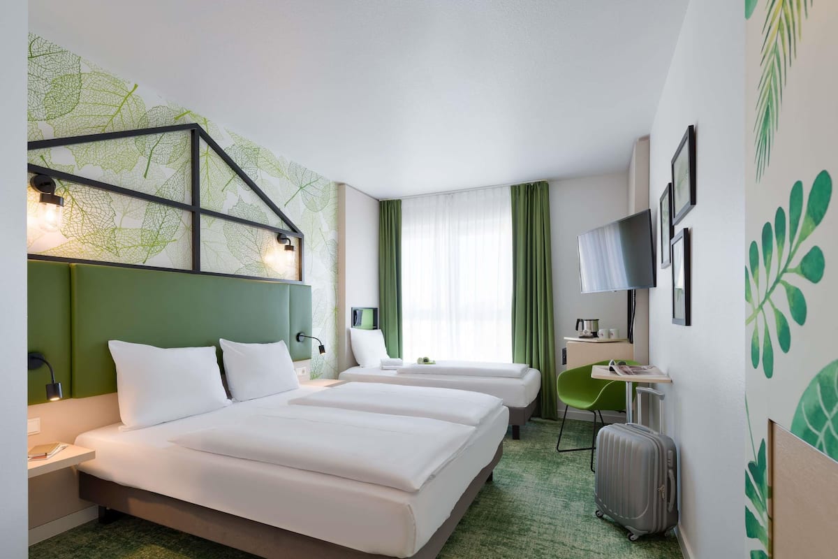 Habitación de hotel con dos camas, un escritorio, un televisor y una alfombra verde.