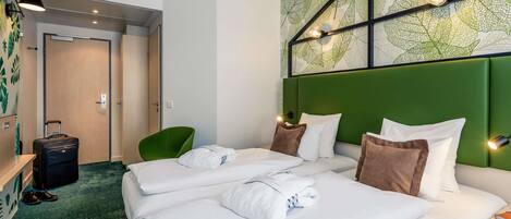 A hotel room with two beds, a green chair, a suitcase, and a wall with a leaf pattern.