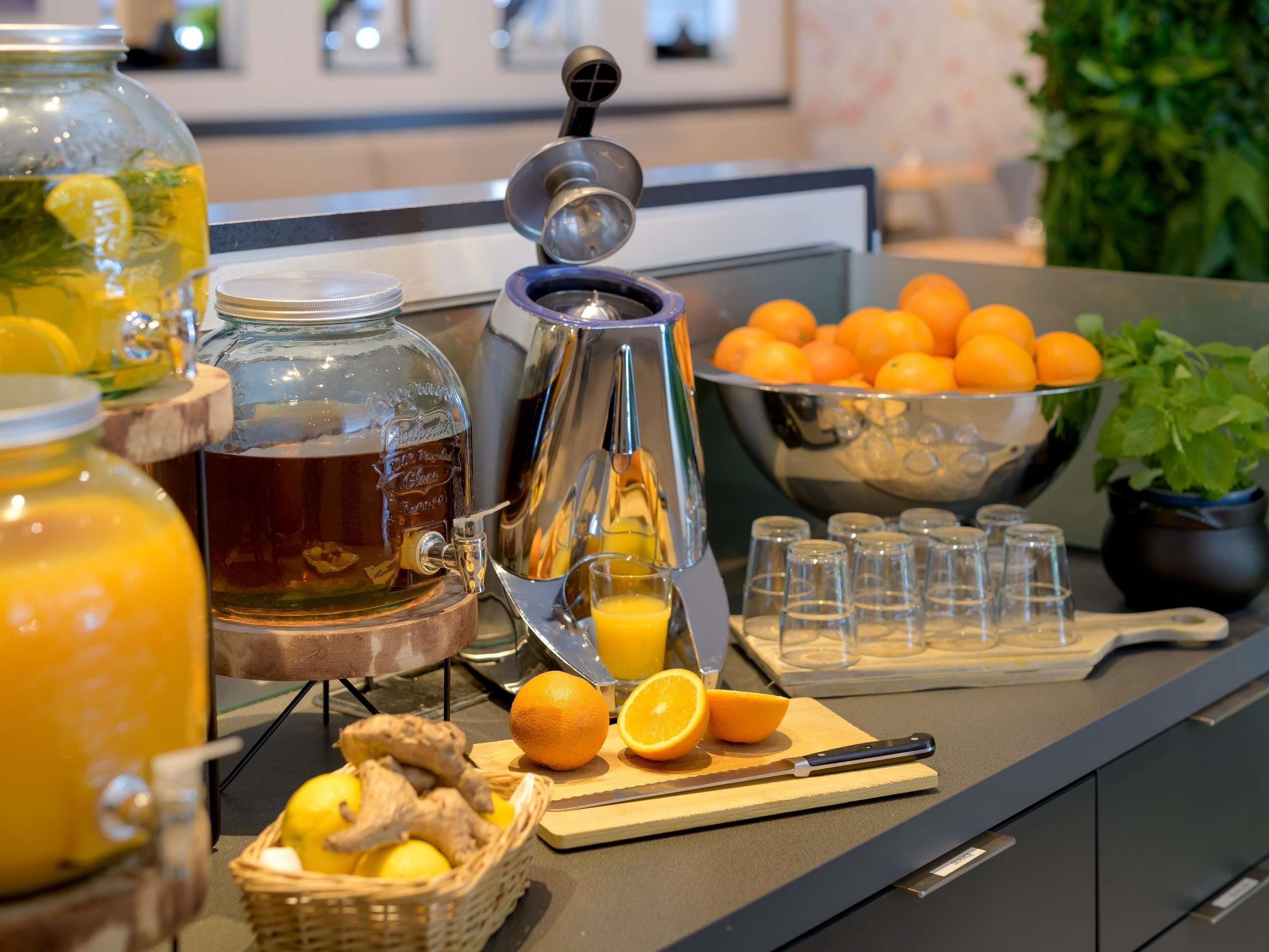A kitchen counter with a coffee maker, a glass jar of tea, a bowl of oranges, and a basket of lemons.