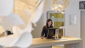 A reception desk with a computer, a lamp, and a signboard with text. - Mercure Hotel Hannover Mitte (Hannover)