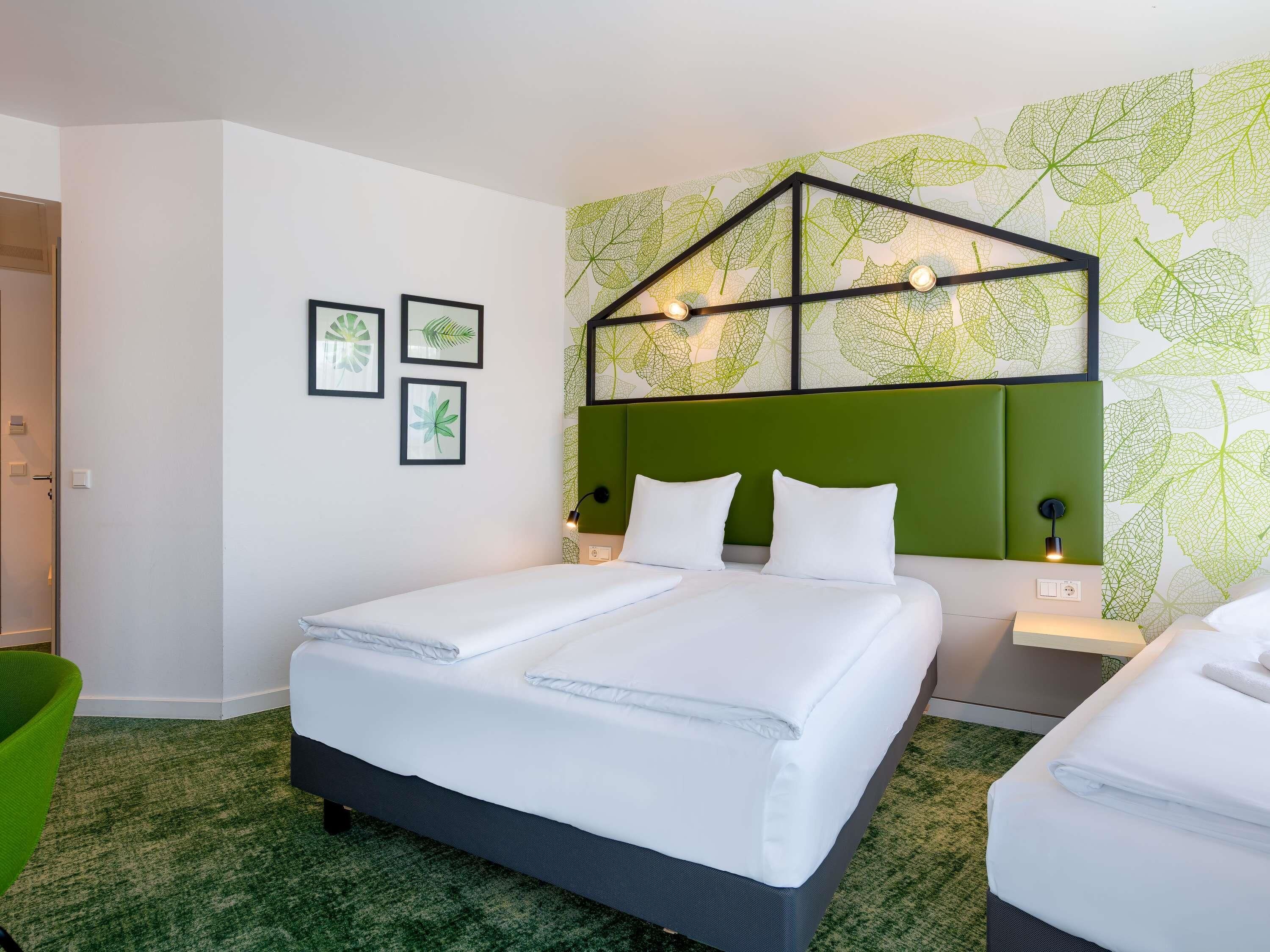 A hotel room with a bed, two bedside tables, a green chair, and a wall with leaf patterns.