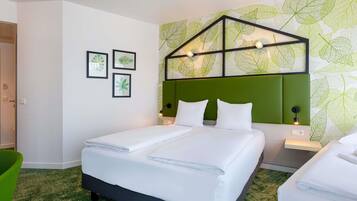 A hotel room with a bed, two bedside tables, a green chair, and a wall with leaf patterns.