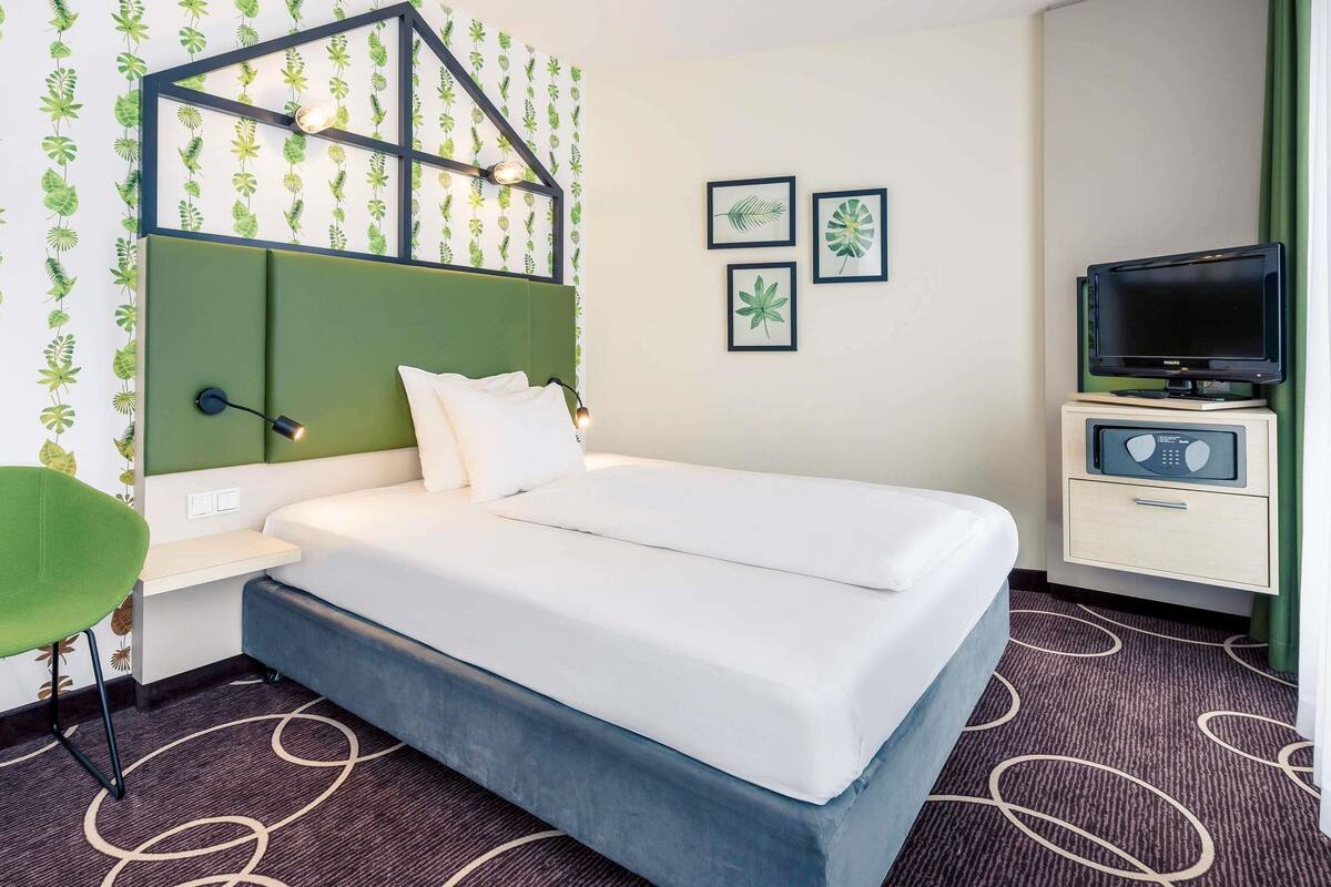 Habitación de hotel con cama, escritorio, televisión y papel tapiz con estampado de hojas.
