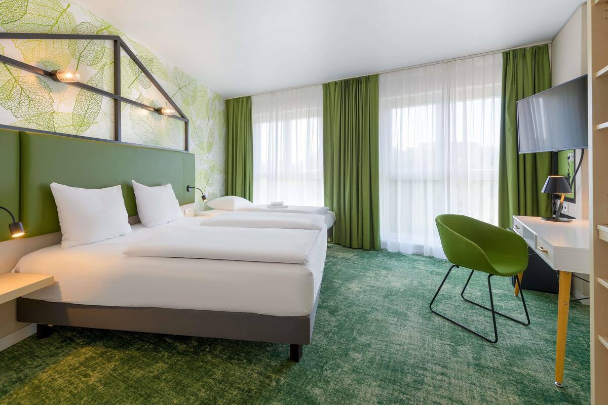 A hotel room with a large bed, a desk with a chair, a TV, and a green carpet.