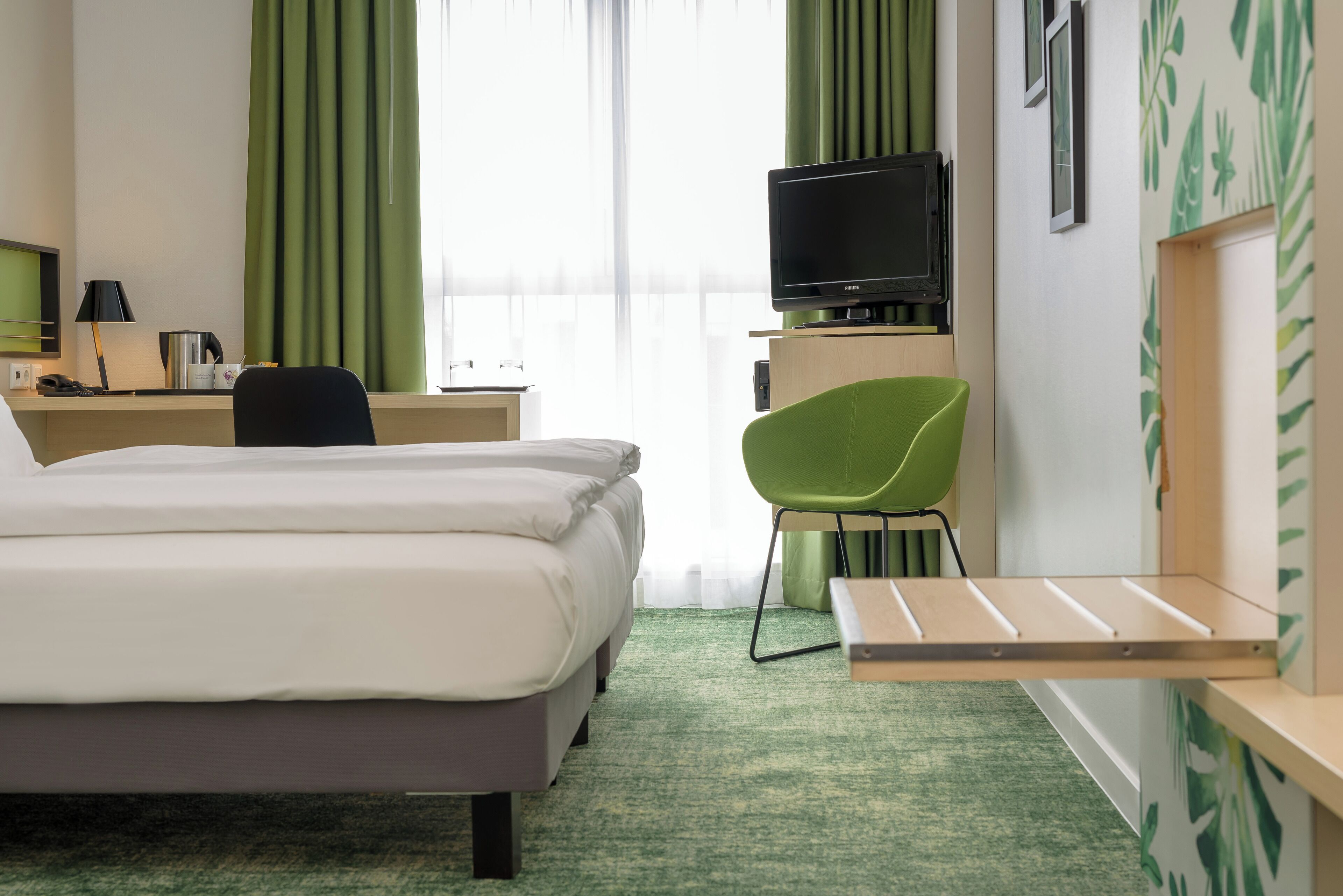 Et hotelværelse med en seng, et skrivebord med en computer, et fjernsyn og en stol.