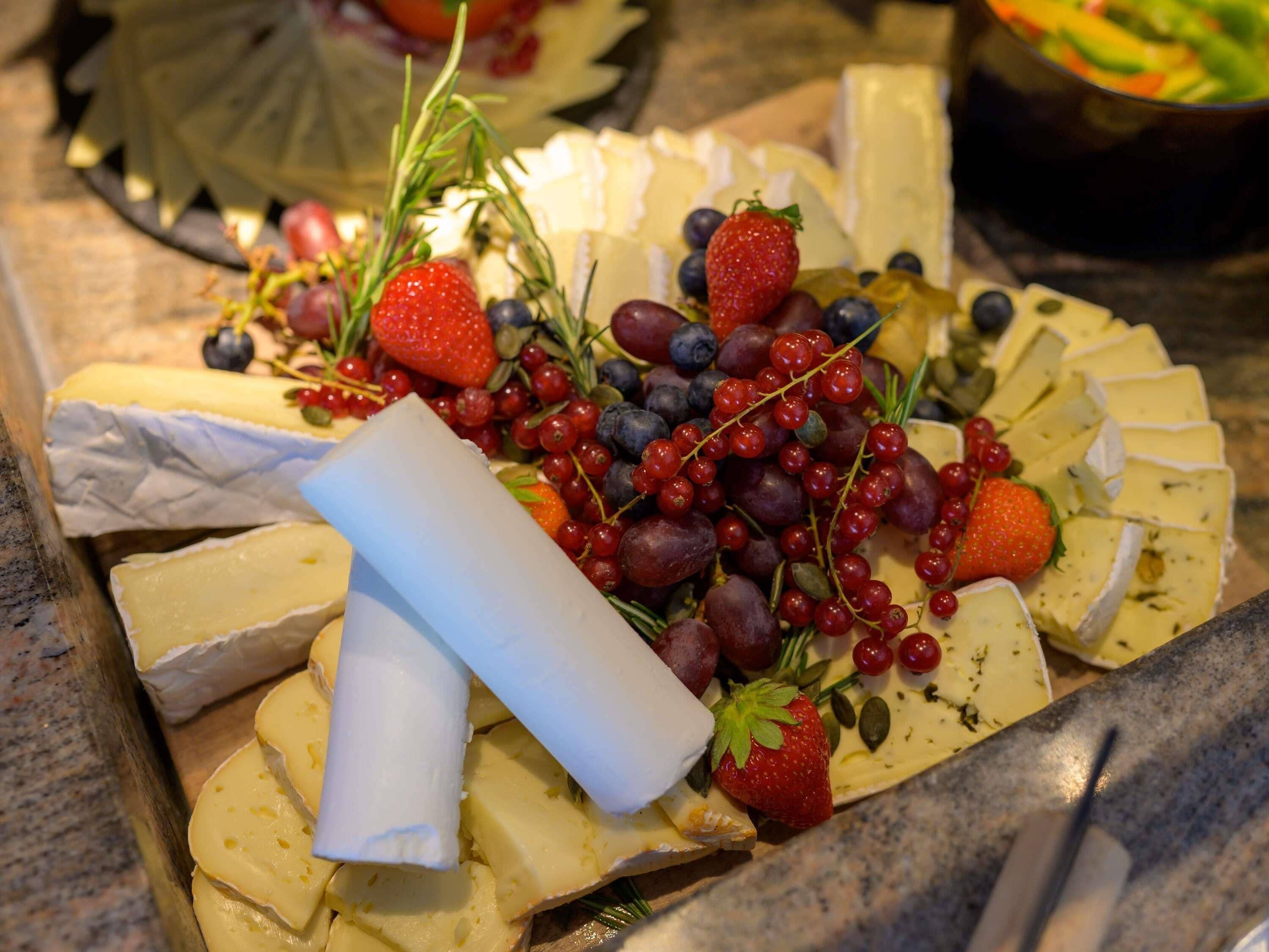 Un plateau de fromages comprenant différents types de fromages et des fruits.