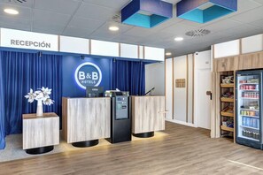 A hotel reception area with a blue curtain backdrop, a reception desk, a minibar, and a refrigerator stocked with beverages.