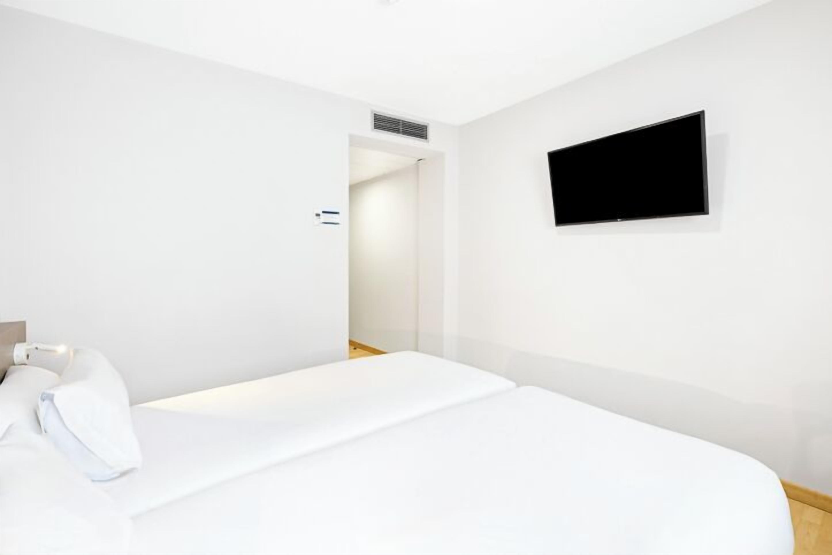 Una habitación de hotel moderna con una cama grande, un televisor de pantalla plana montado en la pared y una puerta visible que da a otra habitación.
