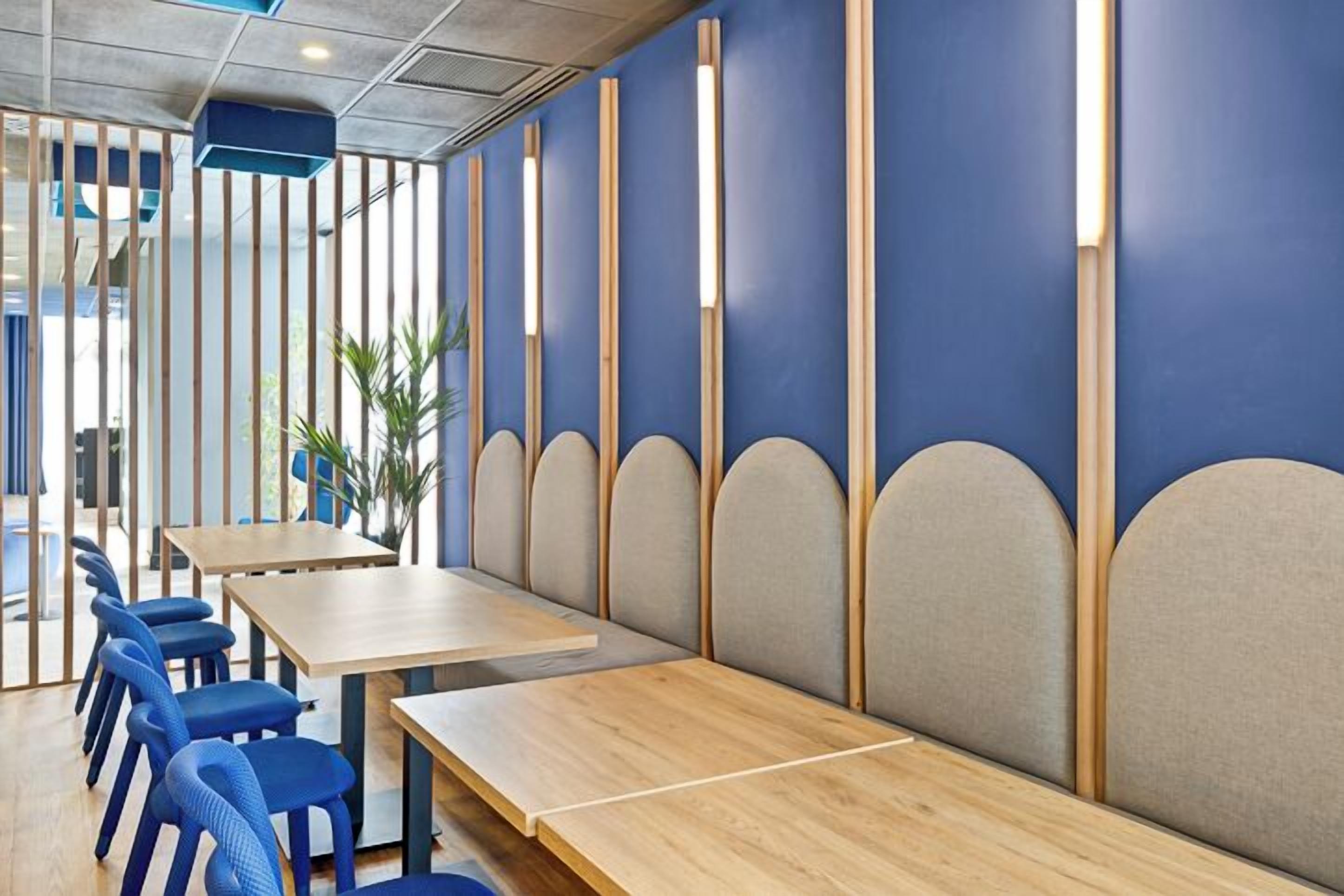 A modern restaurant with wooden tables and blue chairs, featuring a blue and beige color scheme and a partition wall with vertical slats.