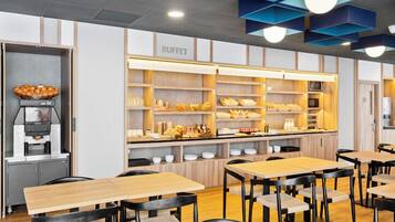Zona de bufé con mesas y sillas de madera, una máquina de café y diferentes alimentos exhibidos en estantes.