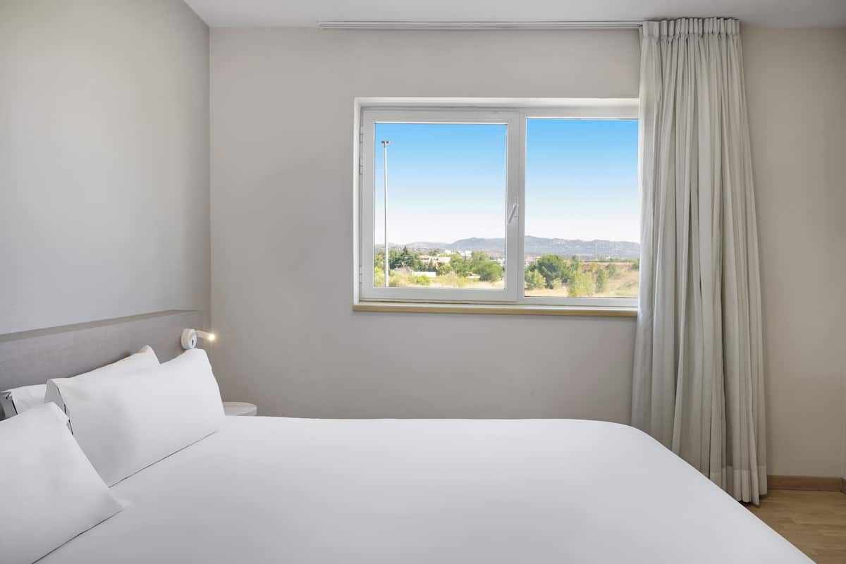 A bedroom with a large bed, a window with a view of the outdoors, and a curtain.