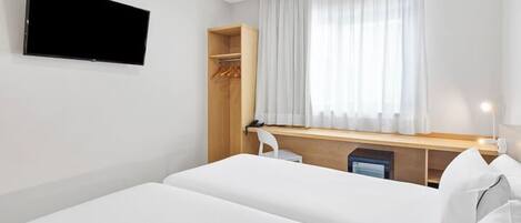 A hotel room with a bed, a desk, a chair, a wardrobe, and a TV mounted on the wall.