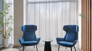 A room with two blue armchairs facing a small round table, a potted plant, and a large window with sheer curtains. - B&B Hotel Las Rozas  (Las Rozas de Madrid)