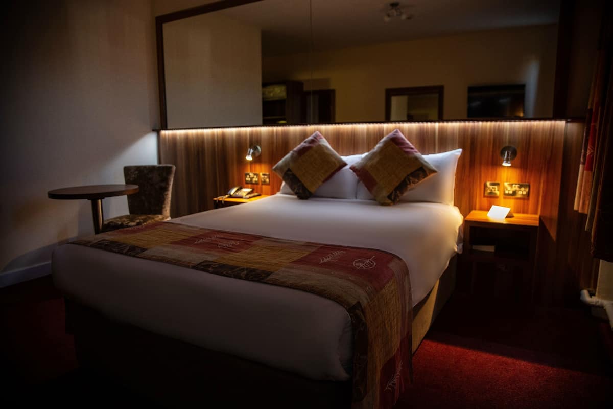 A hotel room with a large bed, two bedside tables with lamps, a chair, and a mirror on the wall.