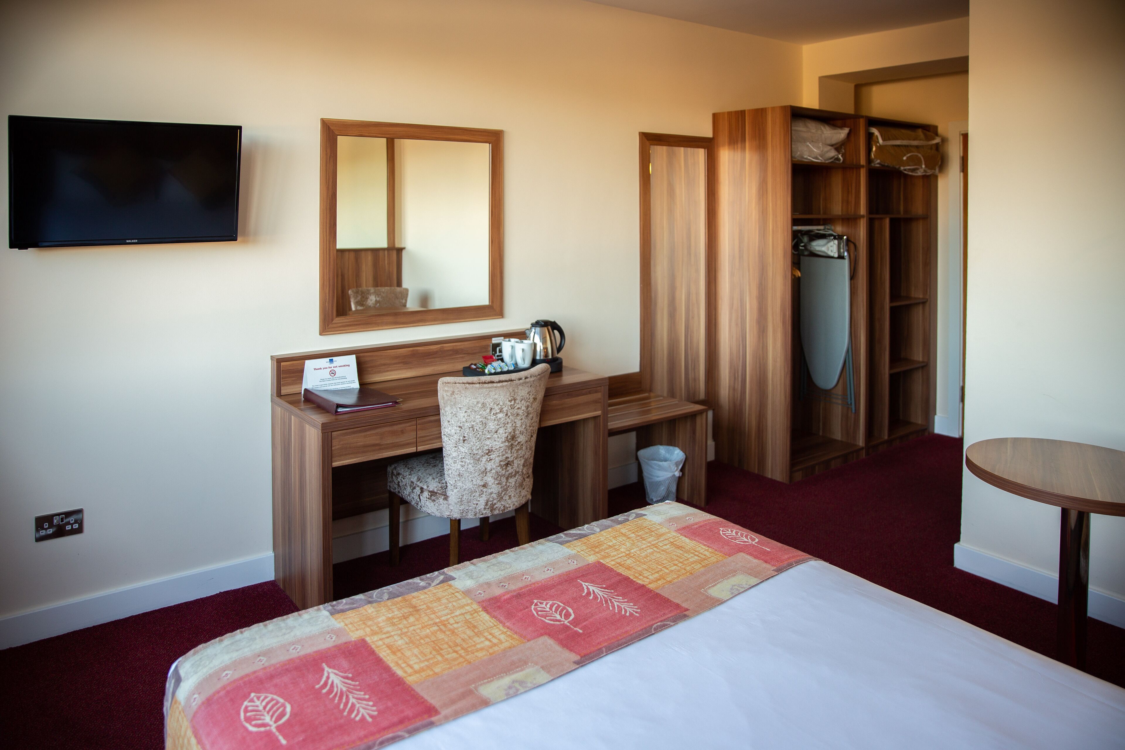 Habitación de hotel con cama, escritorio con silla, televisor, armario y una pequeña mesa redonda.