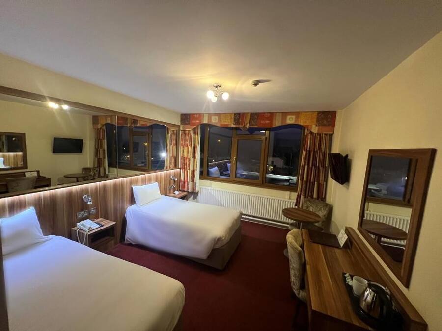 A hotel room with two beds, a desk, a chair, a mirror, and a window.