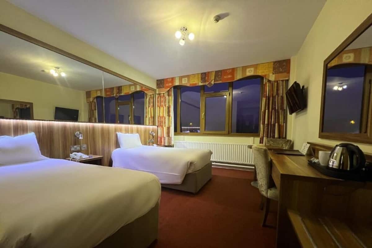 A hotel room with two beds, a desk, a chair, a mirror, and a window with curtains.