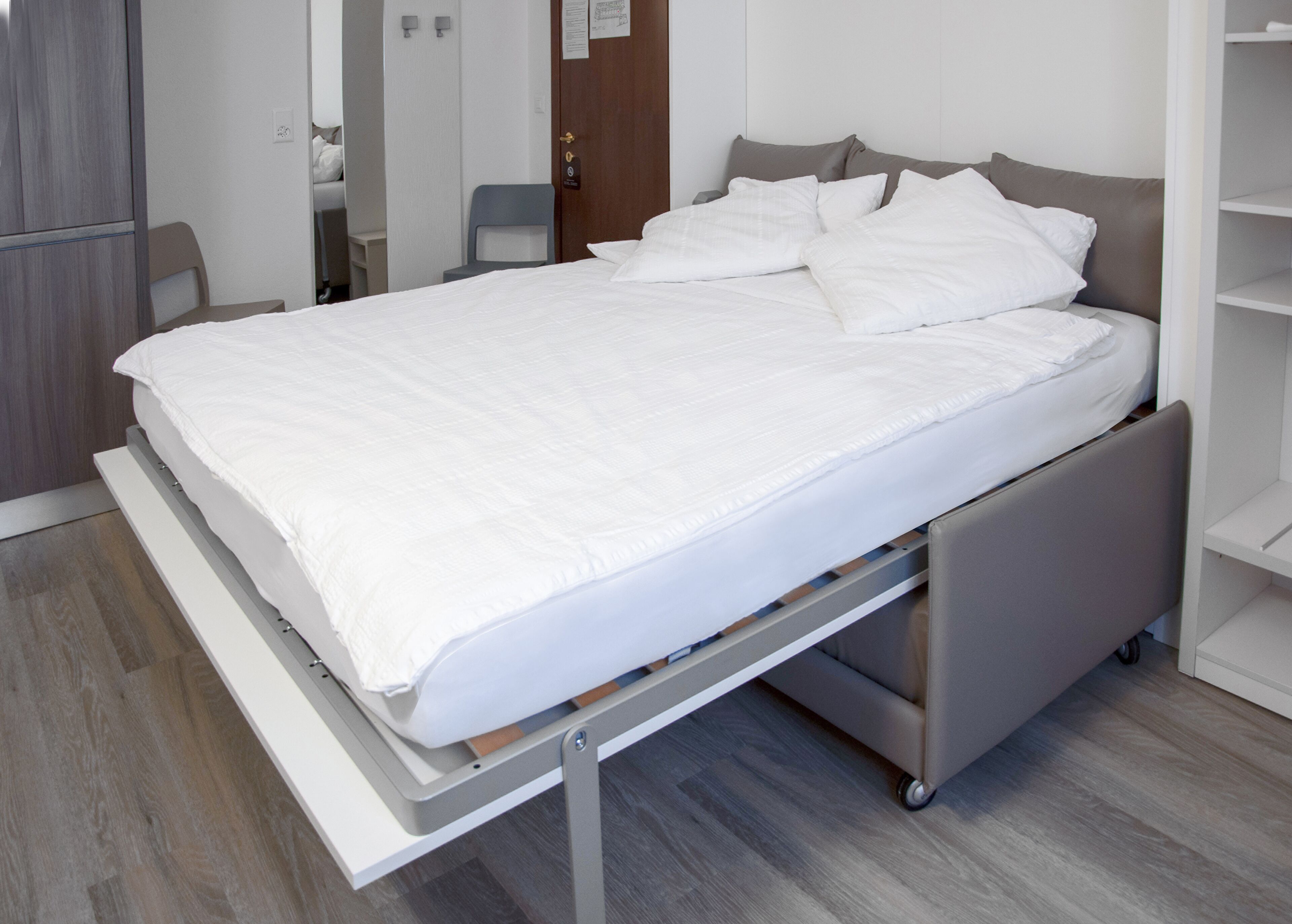 Een modern bed met een metalen frame, witte beddengoed en een grijs hoofdeinde.