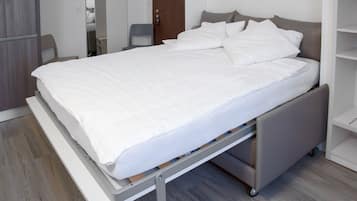 Una cama moderna con estructura metálica, ropa de cama blanca y cabecera gris.