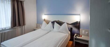 A hotel room with a bed, a nightstand, a lamp, and a painting of a mountain landscape.