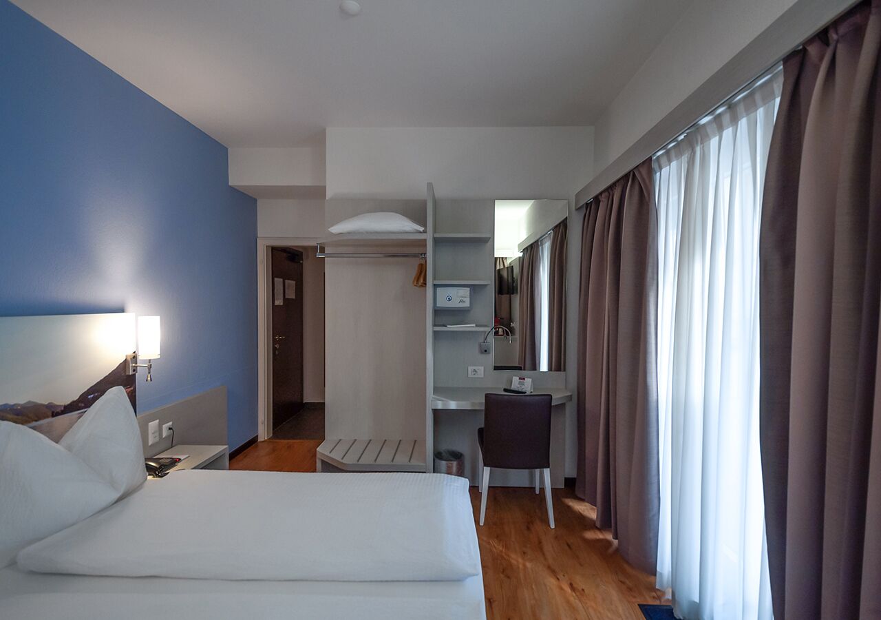 Une chambre d’hôtel comprenant un lit, un bureau, une chaise, un miroir et une armoire.