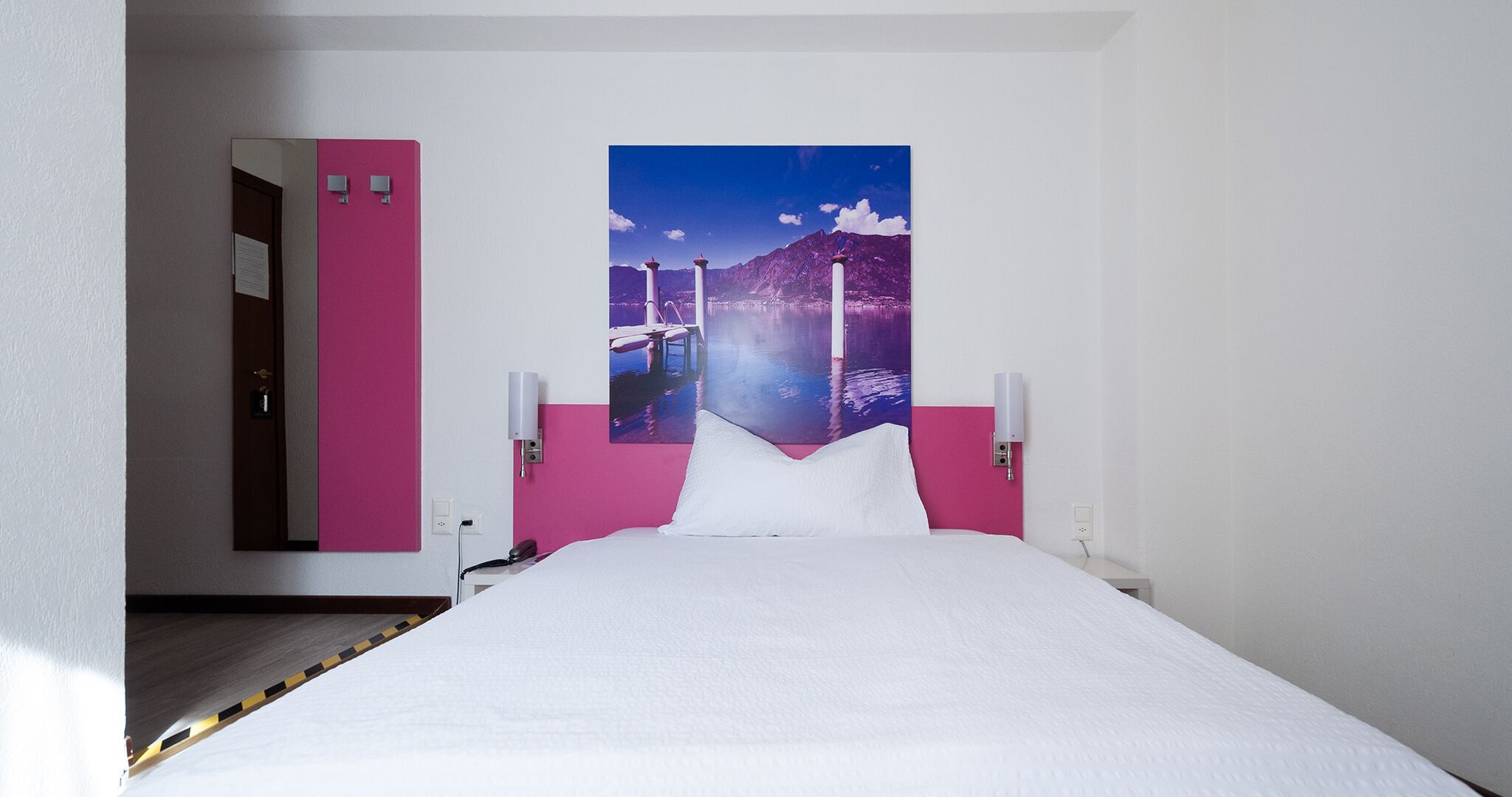 Ein Hotelzimmer mit Bett, großem Fenster und einer rosa Wand.