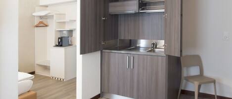 Una cocina compacta con lavamanos integrado, una pequeña encimera y una silla.