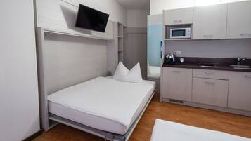 A compact room with a bed, a TV mounted on the wall, a microwave, and a small kitchenette.