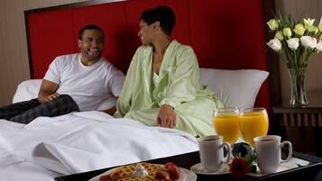 A hotel room with a red headboard, a bed with white linens, a tray with waffles, strawberries, and coffee cups.