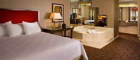 Une chambre d’hôtel avec un grand lit, un coin salon avec une table et des chaises, un grand miroir et une baignoire.