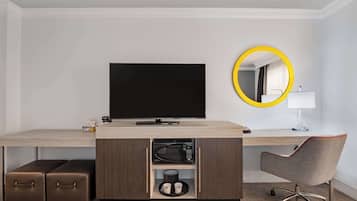 Habitación de hotel con escritorio de madera, televisor de pantalla plana, microondas, cafetera, lámpara y una silla.