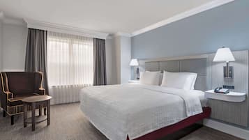 A hotel room with a large bed, a chair, a bedside table with a lamp, and a window with curtains.