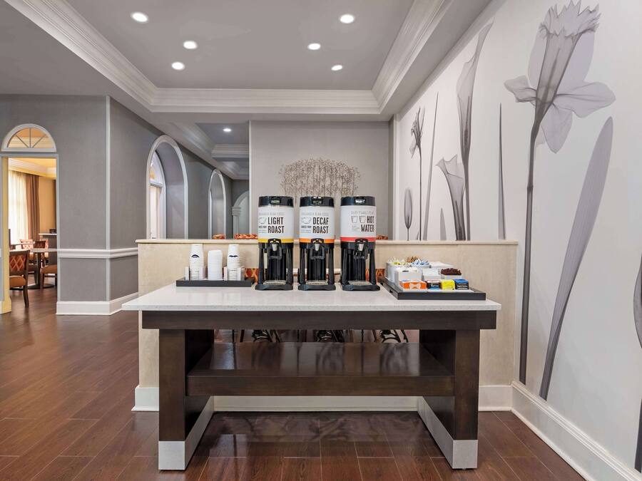 A coffee station with three coffee makers, a tray of disposable cups, and a small selection of snacks.