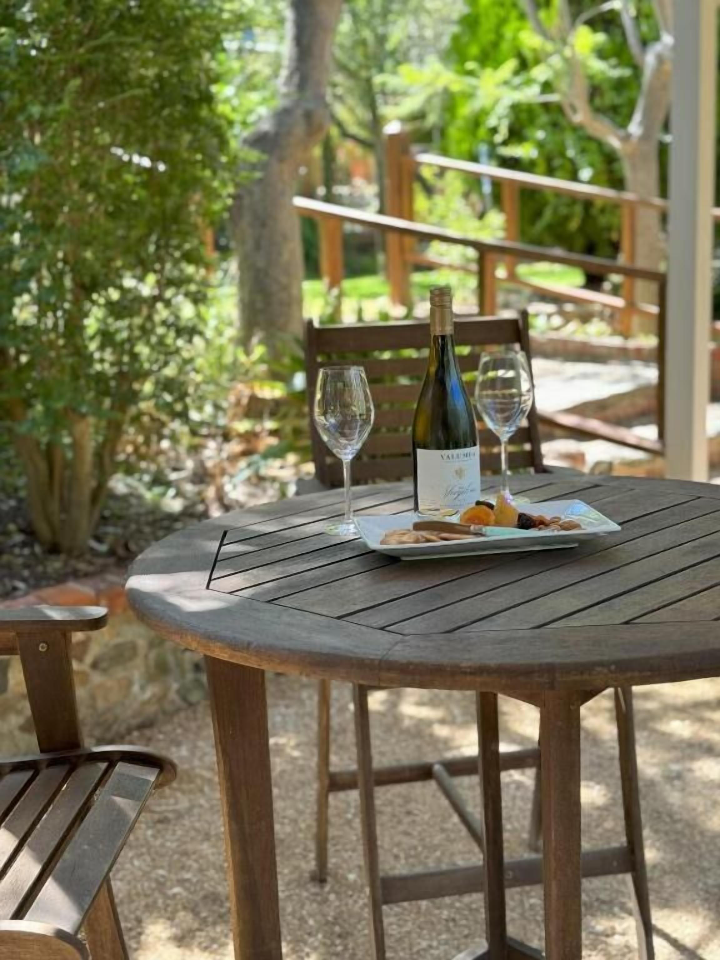 Une table ronde en bois, avec une bouteille de vin, un verre et une assiette de nourriture.