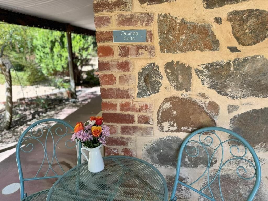 En stenvæg med et skilt, der siger 'Orlando Suite', et metalbord med en hvid vase med blomster, og to metalstole.