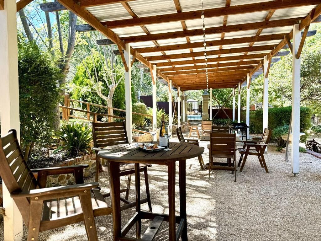 An outdoor patio with wooden furniture, a pergola, and a gravel ground.