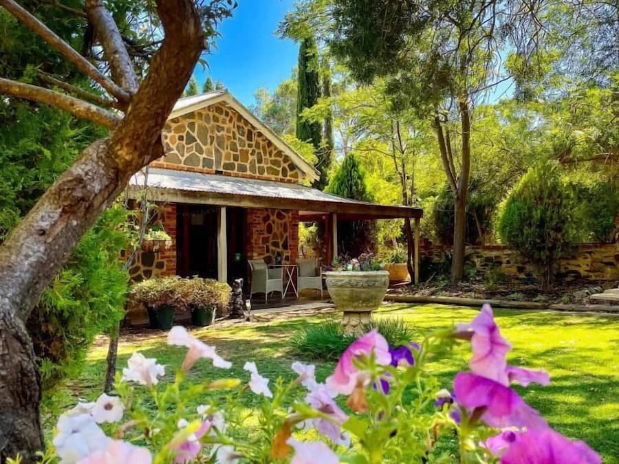 A house with a stone facade, a covered porch, and a garden with flowering plants.
