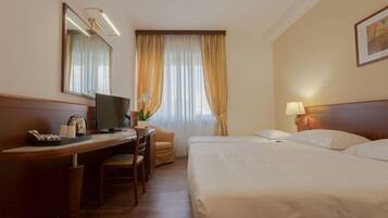 Habitación de hotel con cama, escritorio con computadora, silla, lámpara y ventana con cortinas.