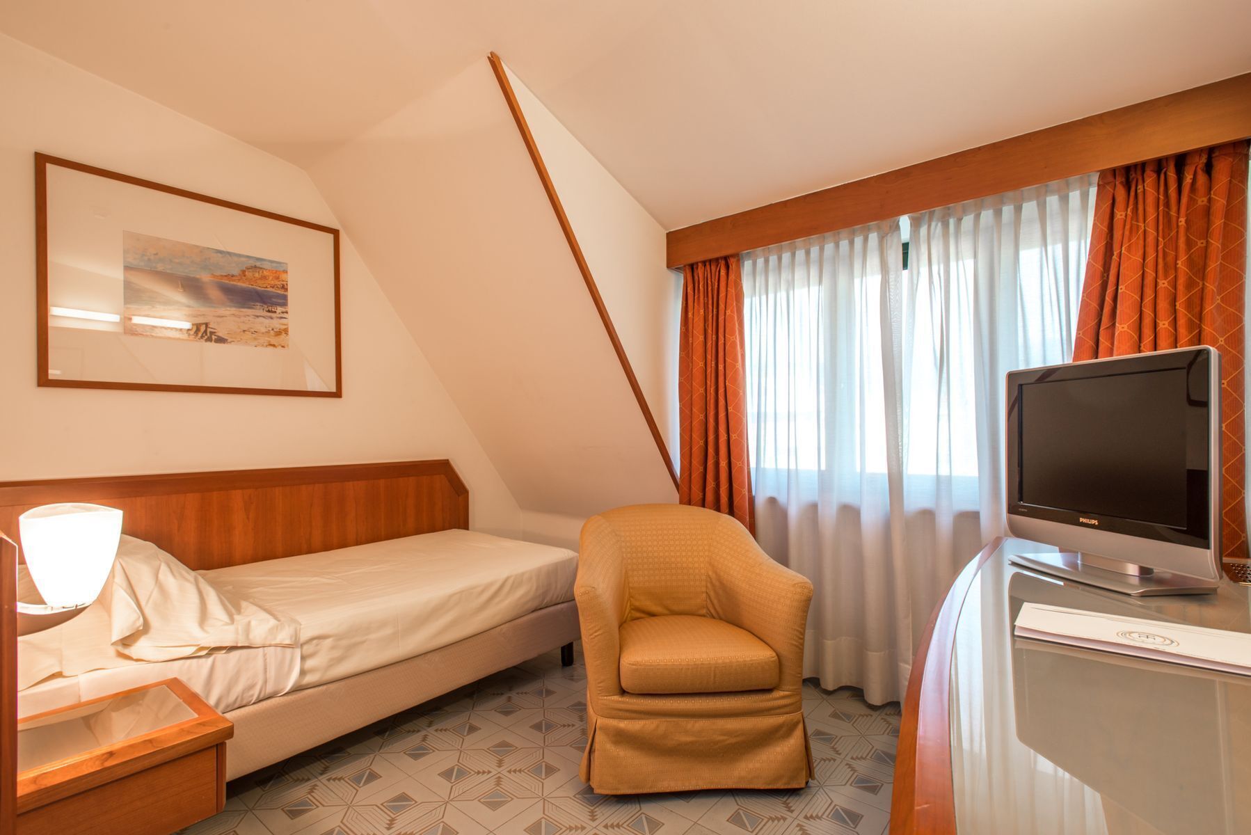 Habitación de hotel con cama, una silla, un escritorio con televisor y un cuadro en la pared.