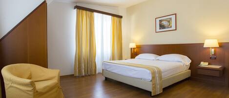 Una habitación de hotel con una cama, una silla, una mesita de noche y un cuadro en la pared.