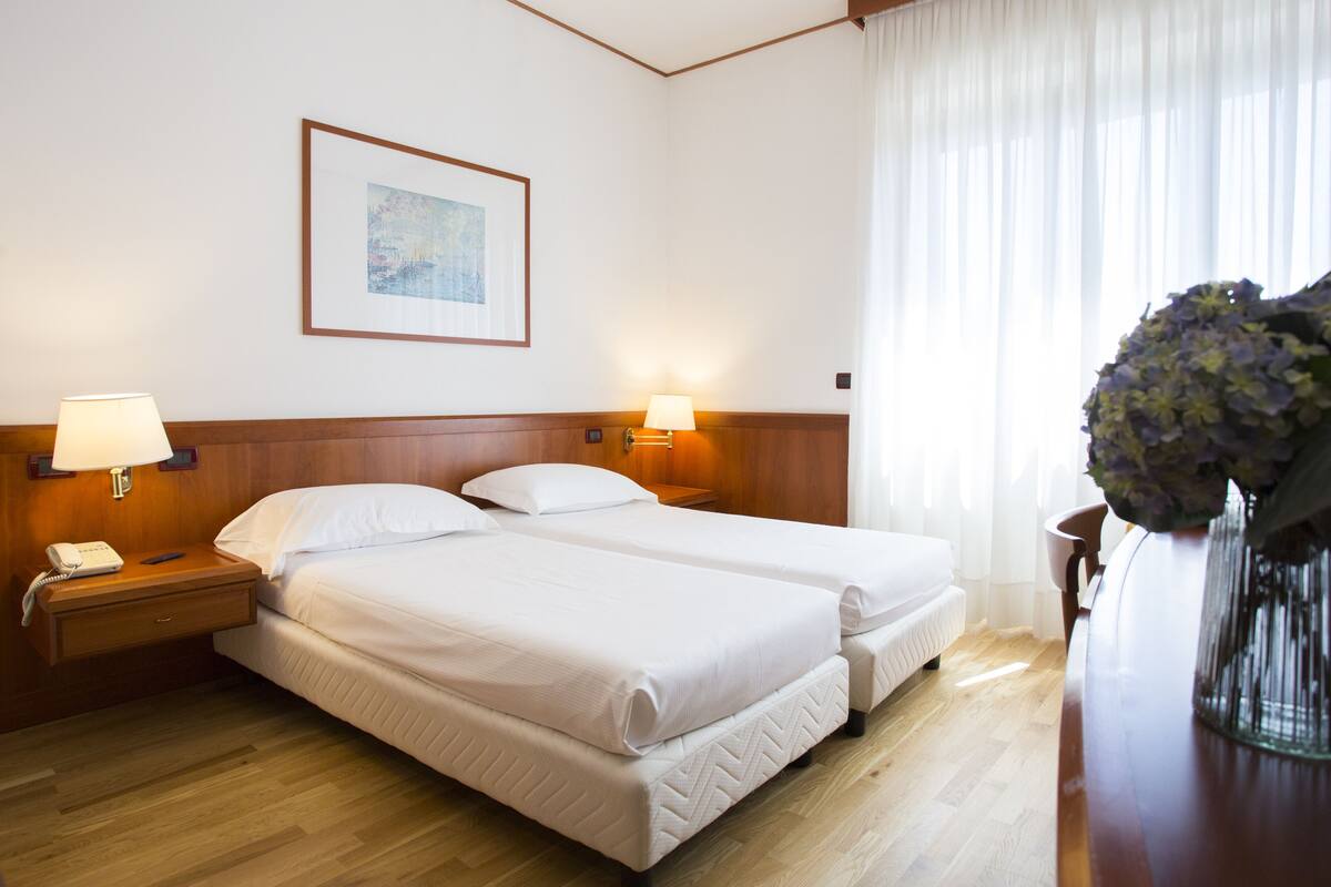 A hotel room with two beds, wooden headboards, bedside lamps, a telephone, and a framed picture on the wall.