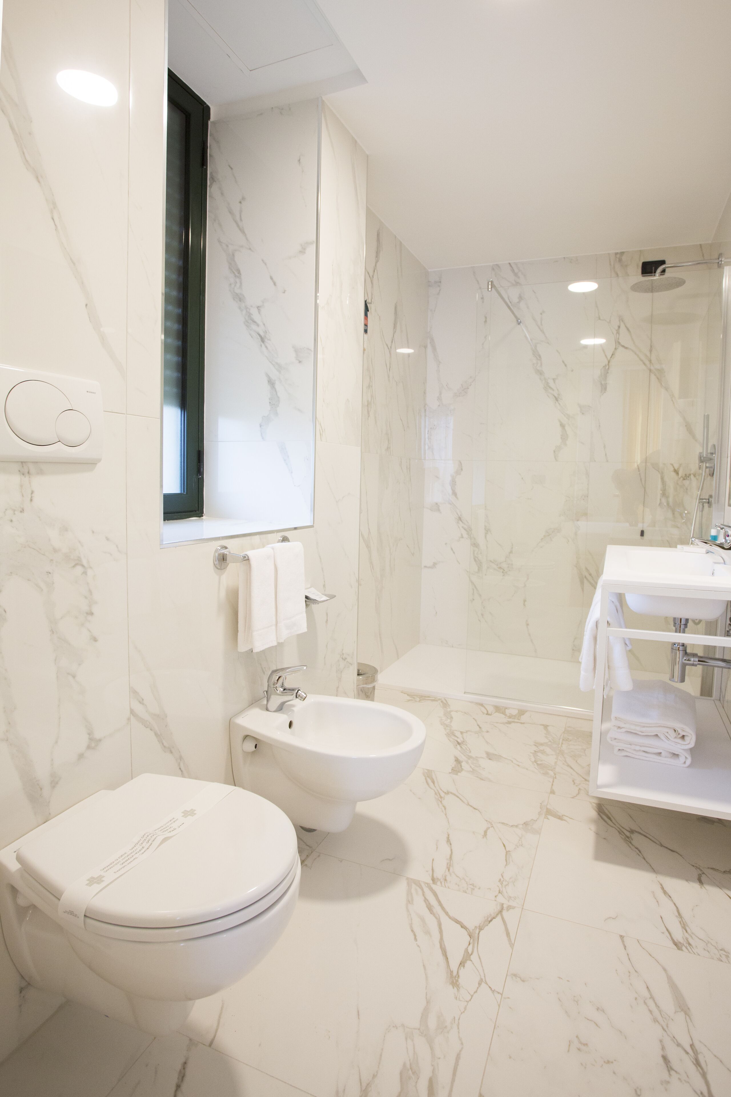 Un baño moderno con inodoro, bidé y lavamanos, todo con paredes y pisos de mármol.