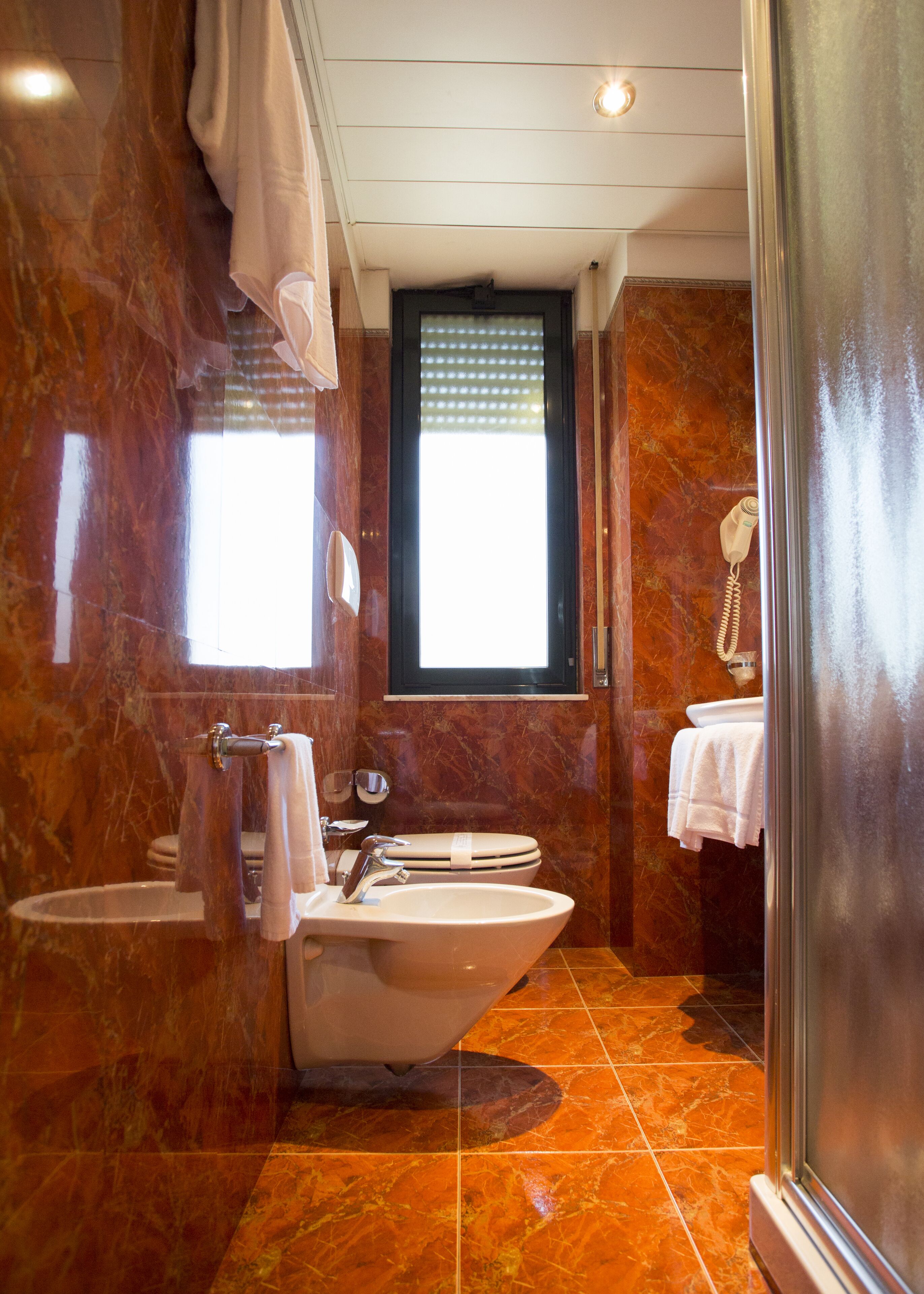 A bathroom with a freestanding bathtub, a sink, and a toilet. There is a window with blinds, a towel rack, and a shower curtain rod.
