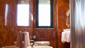 A bathroom with a freestanding bathtub, a sink, and a toilet. There is a window with blinds, a towel rack, and a shower curtain rod.