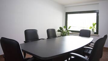 Un salón de conferencias con una larga mesa y seis sillas, una ventana con vistas y dos plantas en macetas.