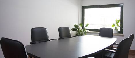 Uma sala de conferências com uma mesa comprida e seis cadeiras, uma janela com vista e duas plantas em vasos.