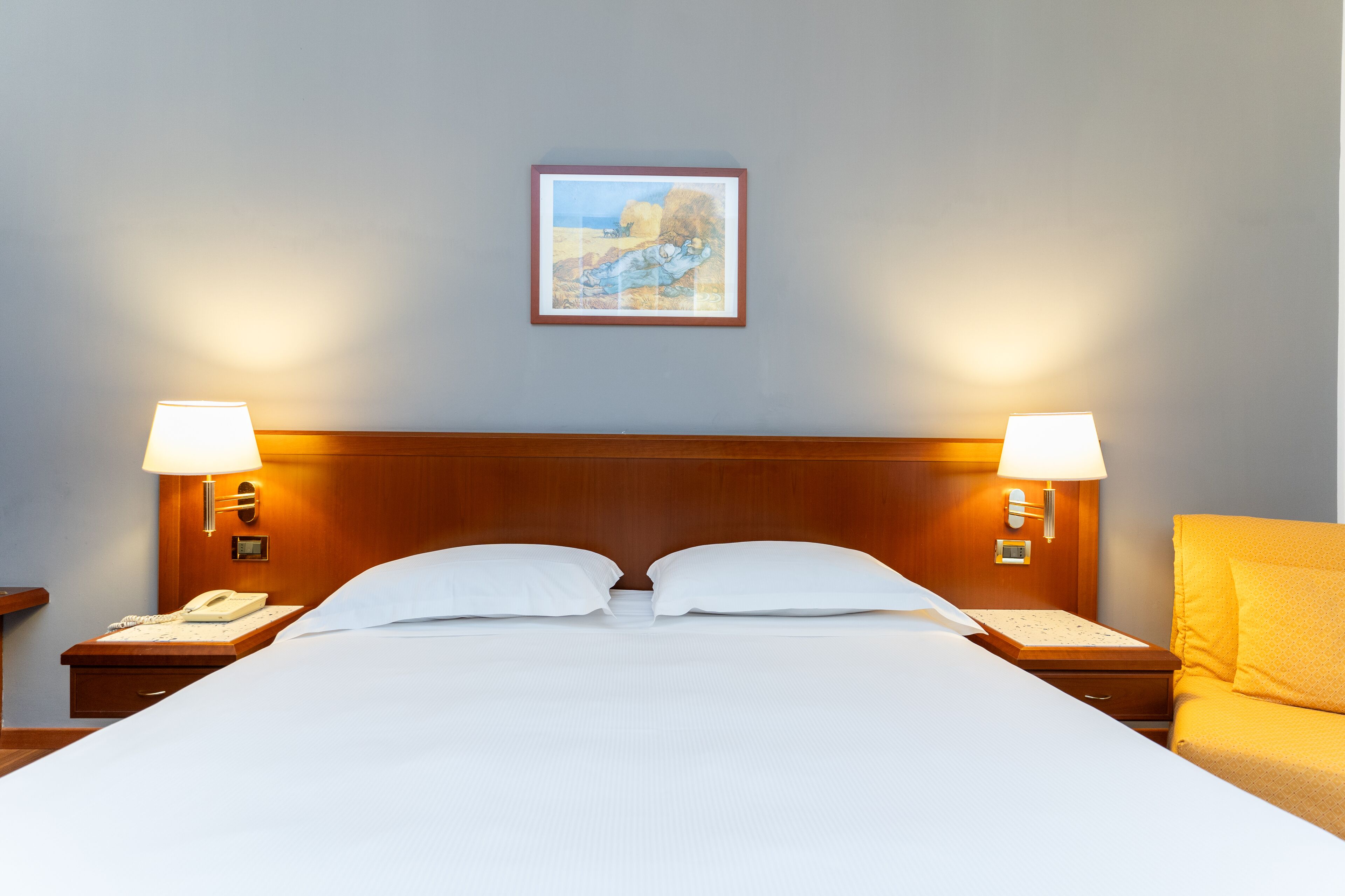 Un cuarto de hotel con una cama grande, dos lámparas de noche, un mesita de noche con un teléfono y un cuadro en la pared.